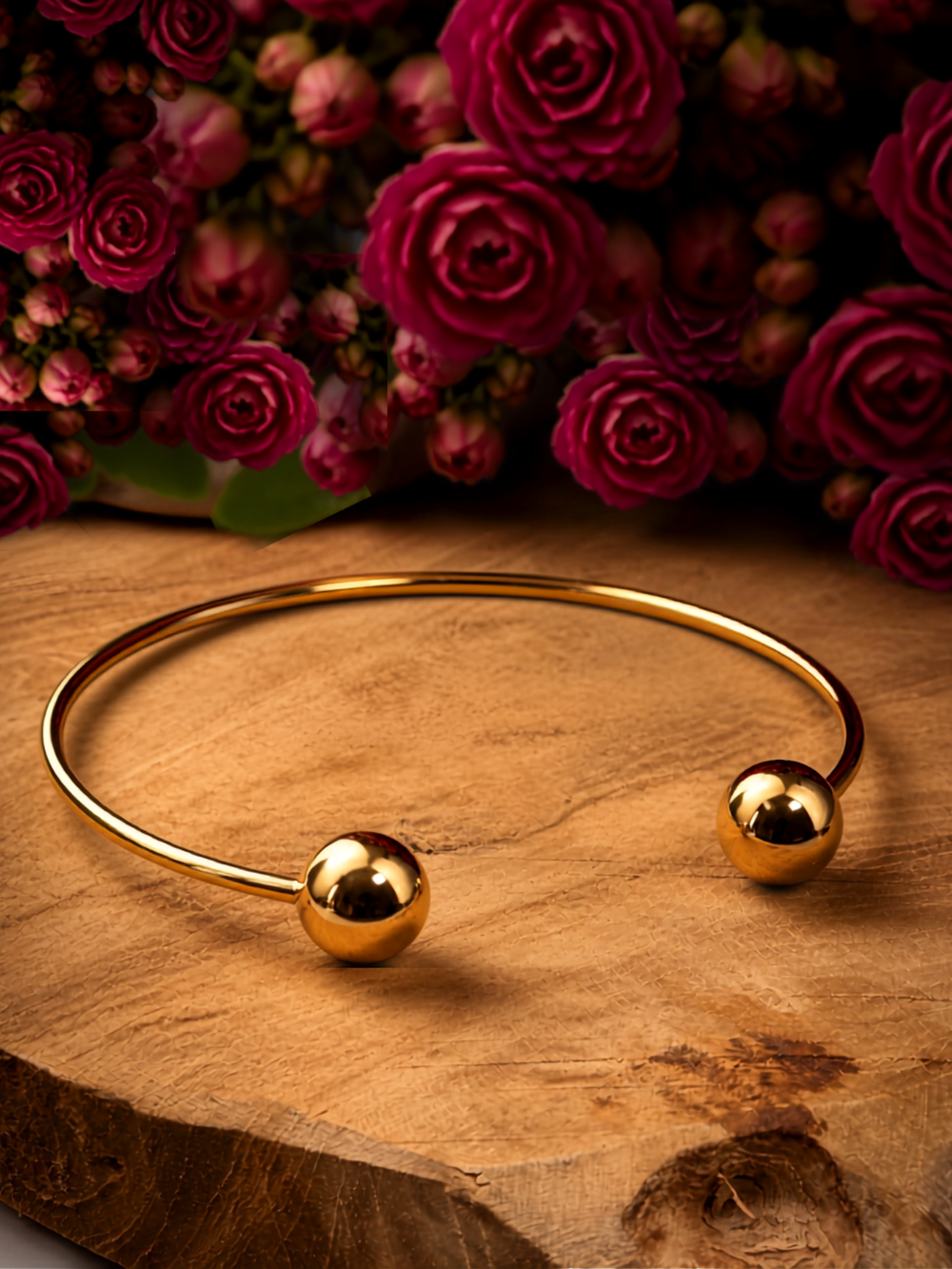 Armreif in goldfarben mit Kugeln, liegend auf einem Holzstück